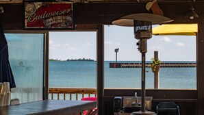 Vue prise depuis le pont d’un bateau, avec une rambarde en bois, une table ornée d’une enseigne Budweiser, et une vue sur l’eau et un quai au loin.