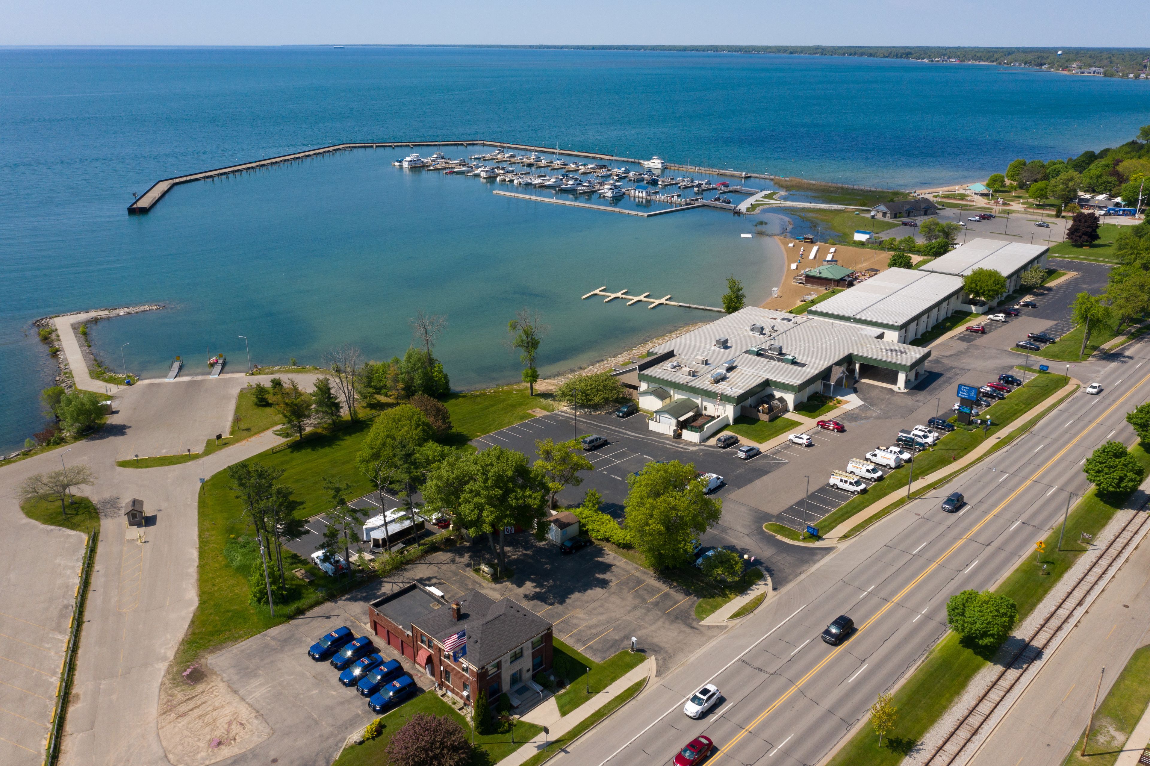 An aerial view of a marina with boats docked, a parking lot, and a building with a green roof.