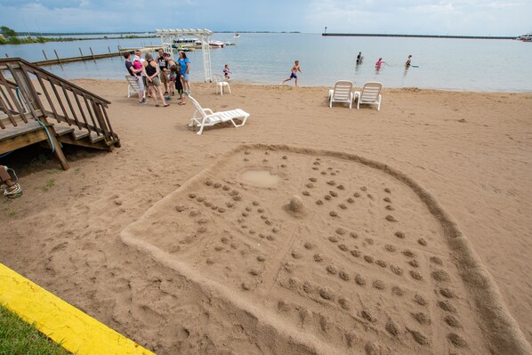 Una playa con una escultura de arena con forma de mano, una pasarela de madera y un muelle al fondo.