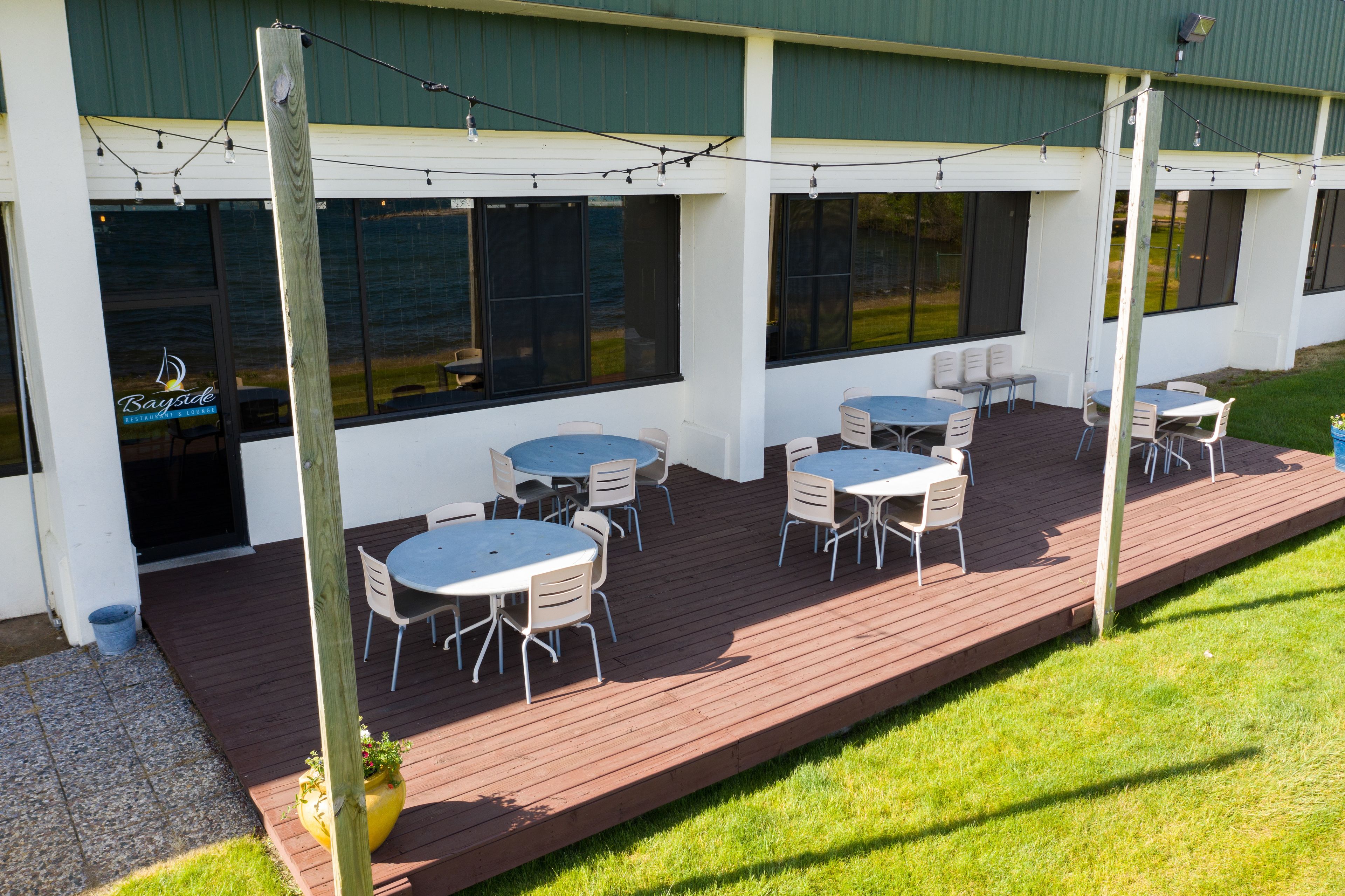 An outdoor patio with multiple round tables and chairs, a wooden deck, and string lights.