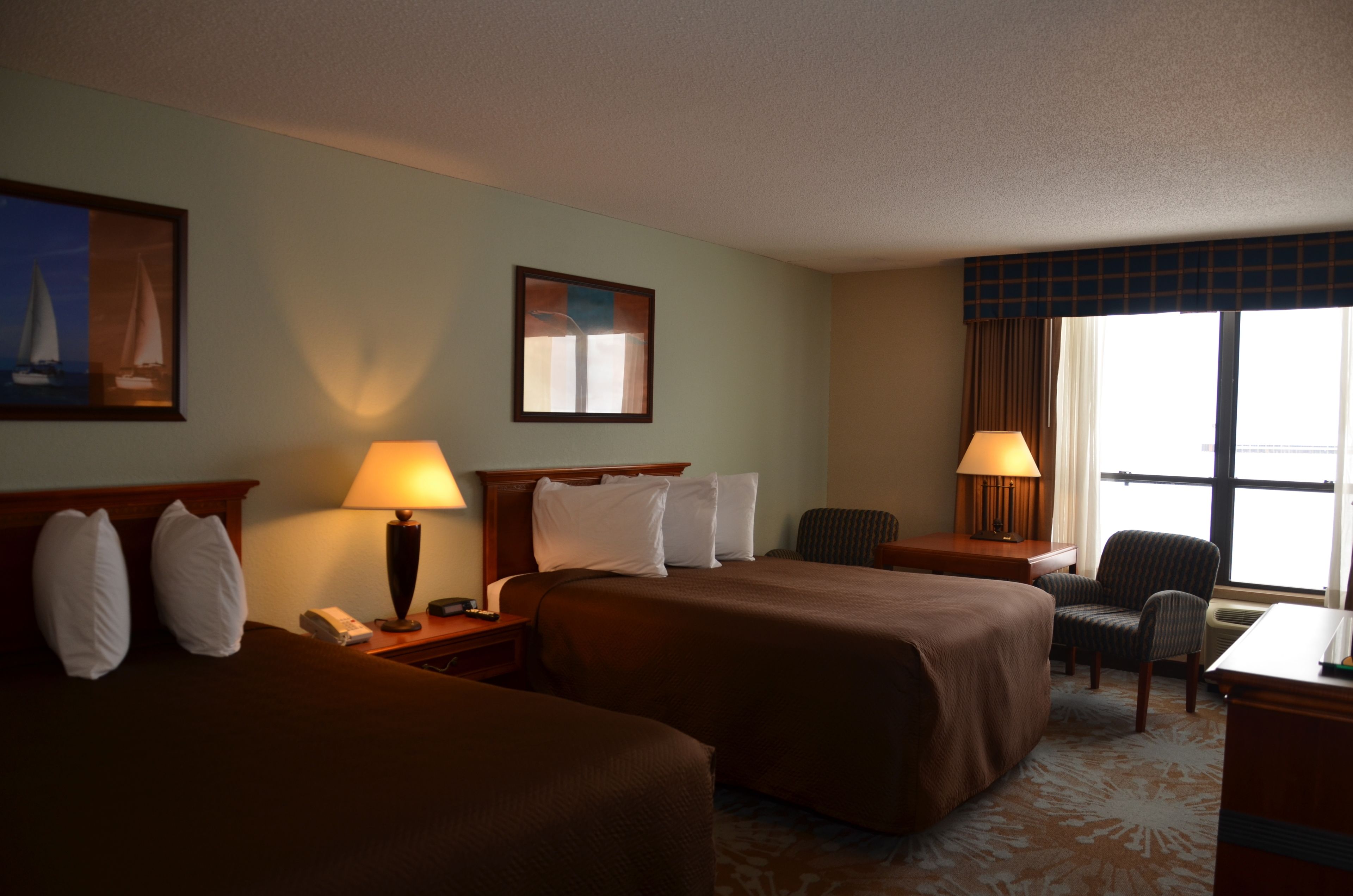 A hotel room with two beds, a desk, a chair, and a window with curtains.