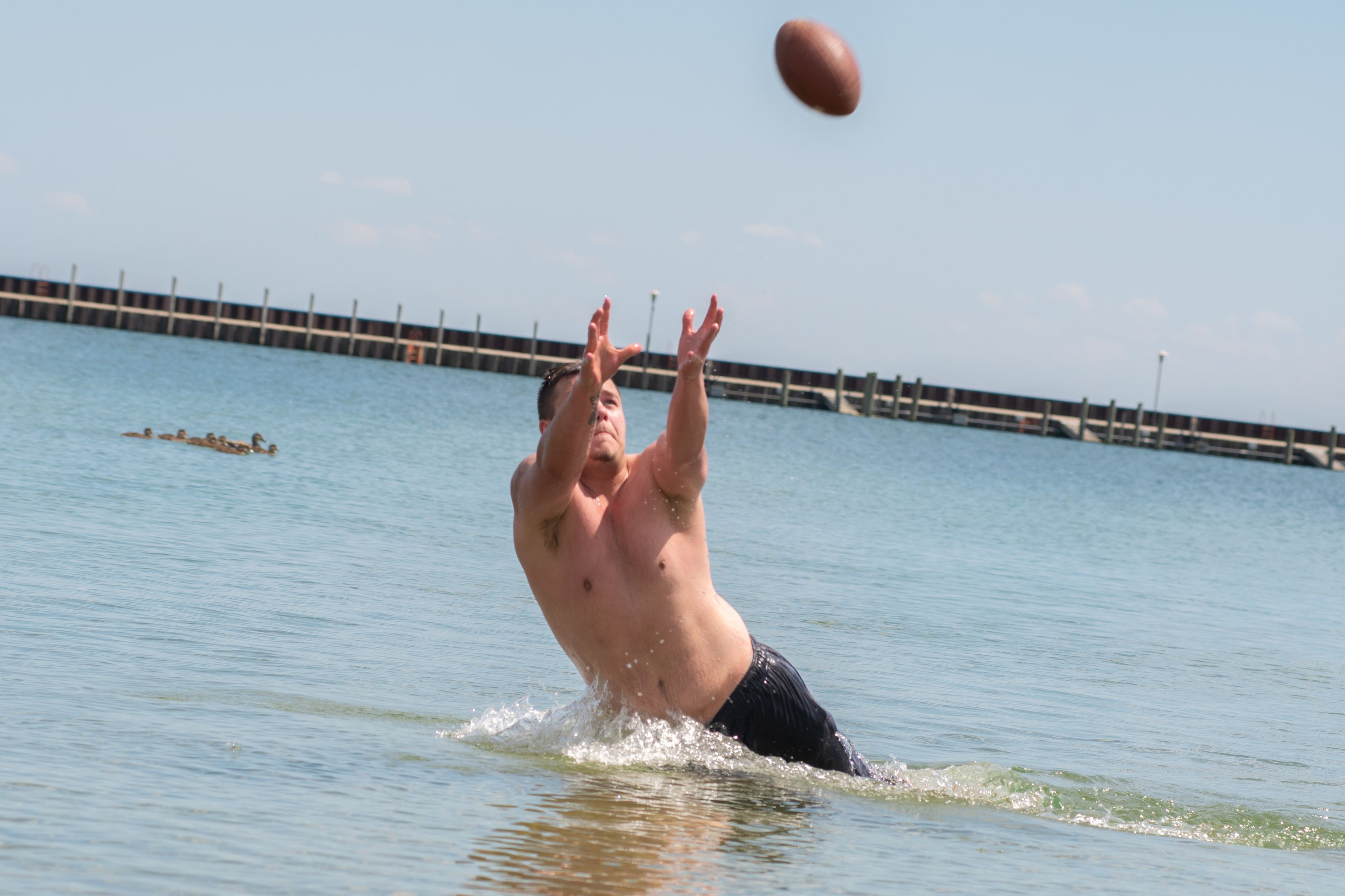 A man playing football in a body of water with a pier in the background.