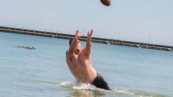 A man playing football in a body of water with a pier in the background.