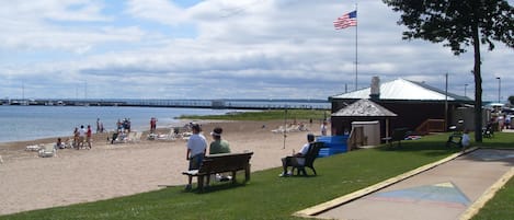 A beach with a pier in the background, a small building with a flag, and people relaxing on the sand.