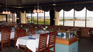 Un restaurant offrant une vue sur l’eau, avec des chaises en bois, des tables recouvertes de nappes blanches et des lampes suspendues.