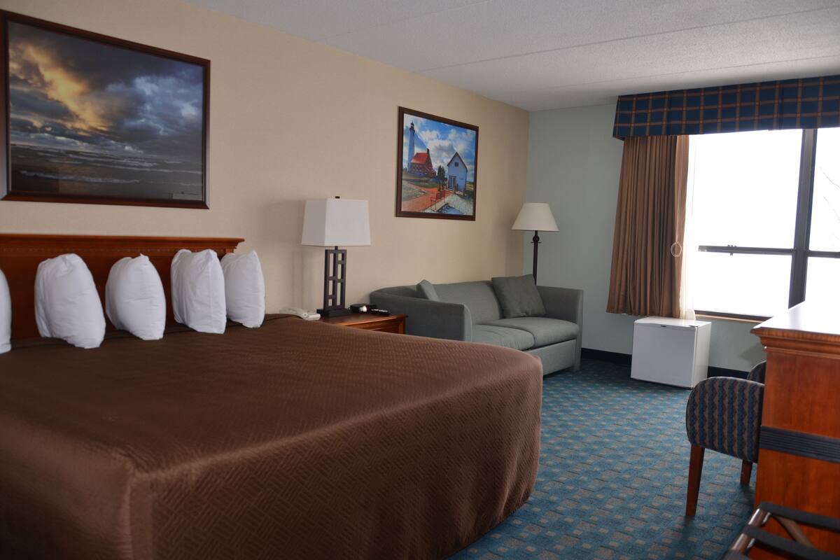 Une chambre d’hôtel avec un grand lit, un canapé gris, un bureau et une fenêtre avec des rideaux.