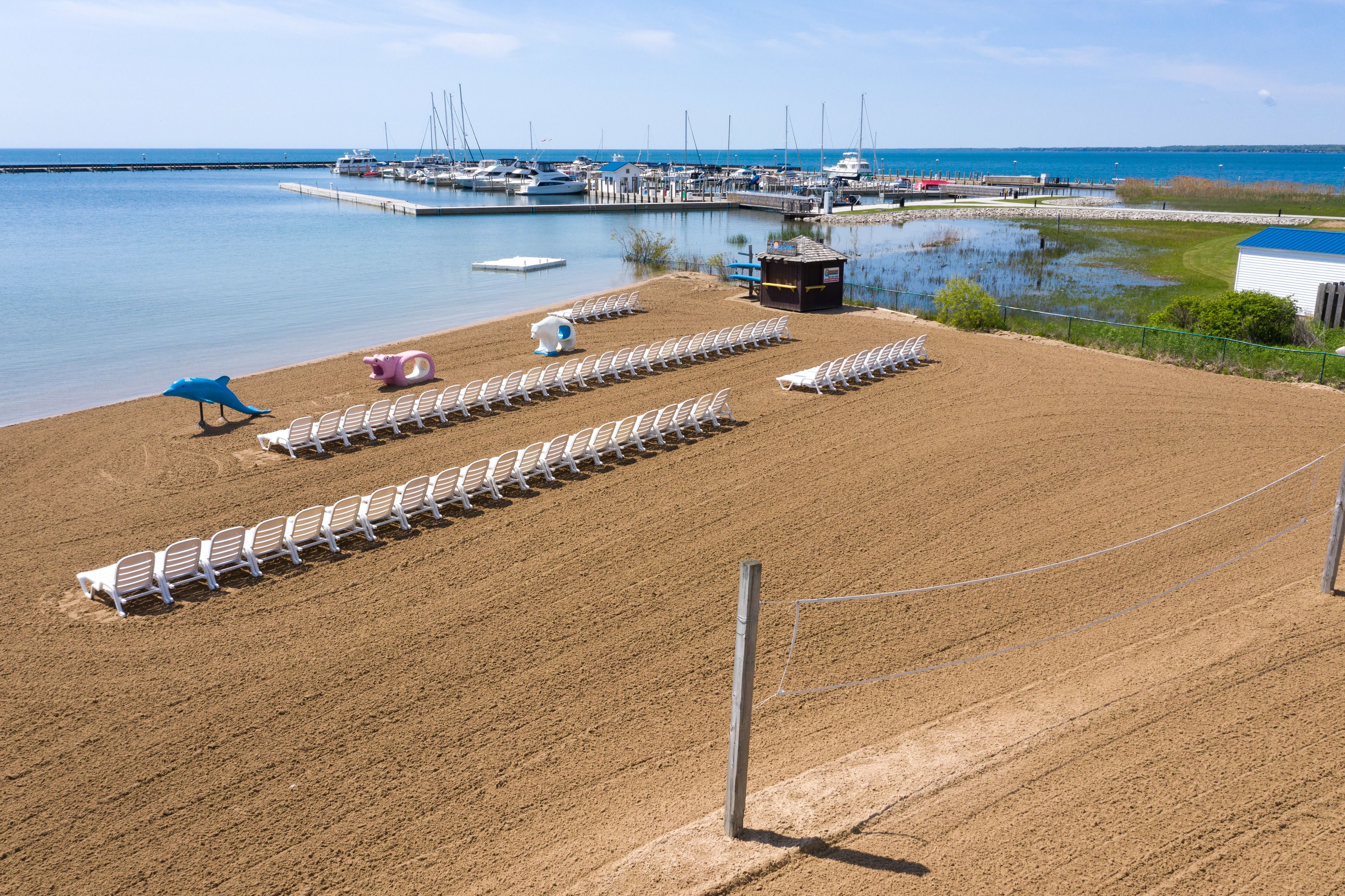 A sandy beach with rows of white lounge chairs and a small blue bird sculpture.