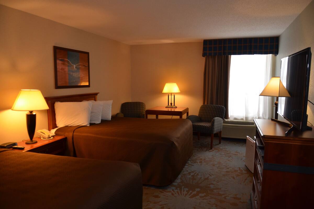 Une chambre d’hôtel avec deux lits, un bureau, une chaise, une télévision et une lampe.