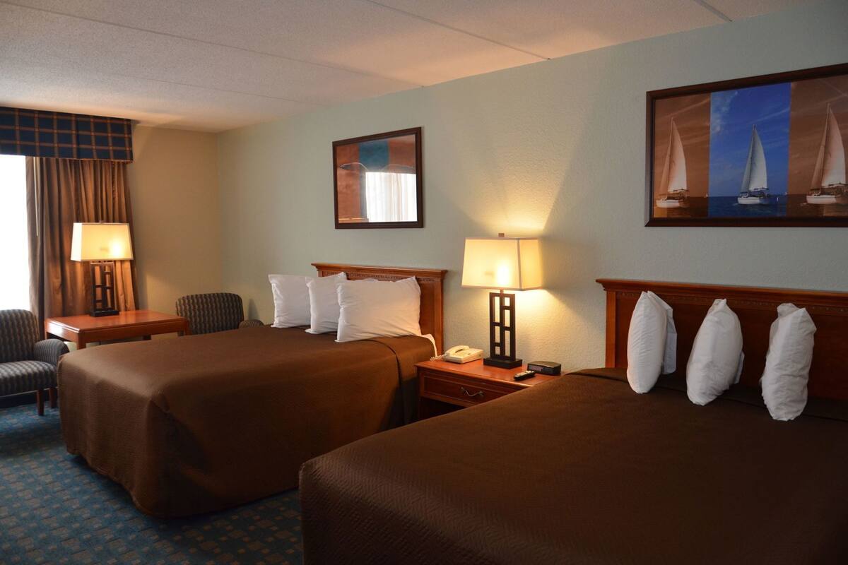 Une chambre d’hôtel avec deux lits, un bureau, une chaise, une lampe et un tableau au mur.