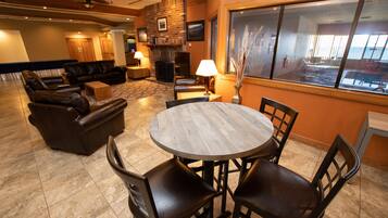 A cozy living area with leather sofas, a round wooden table, and chairs. A fireplace and a TV are visible in the background.