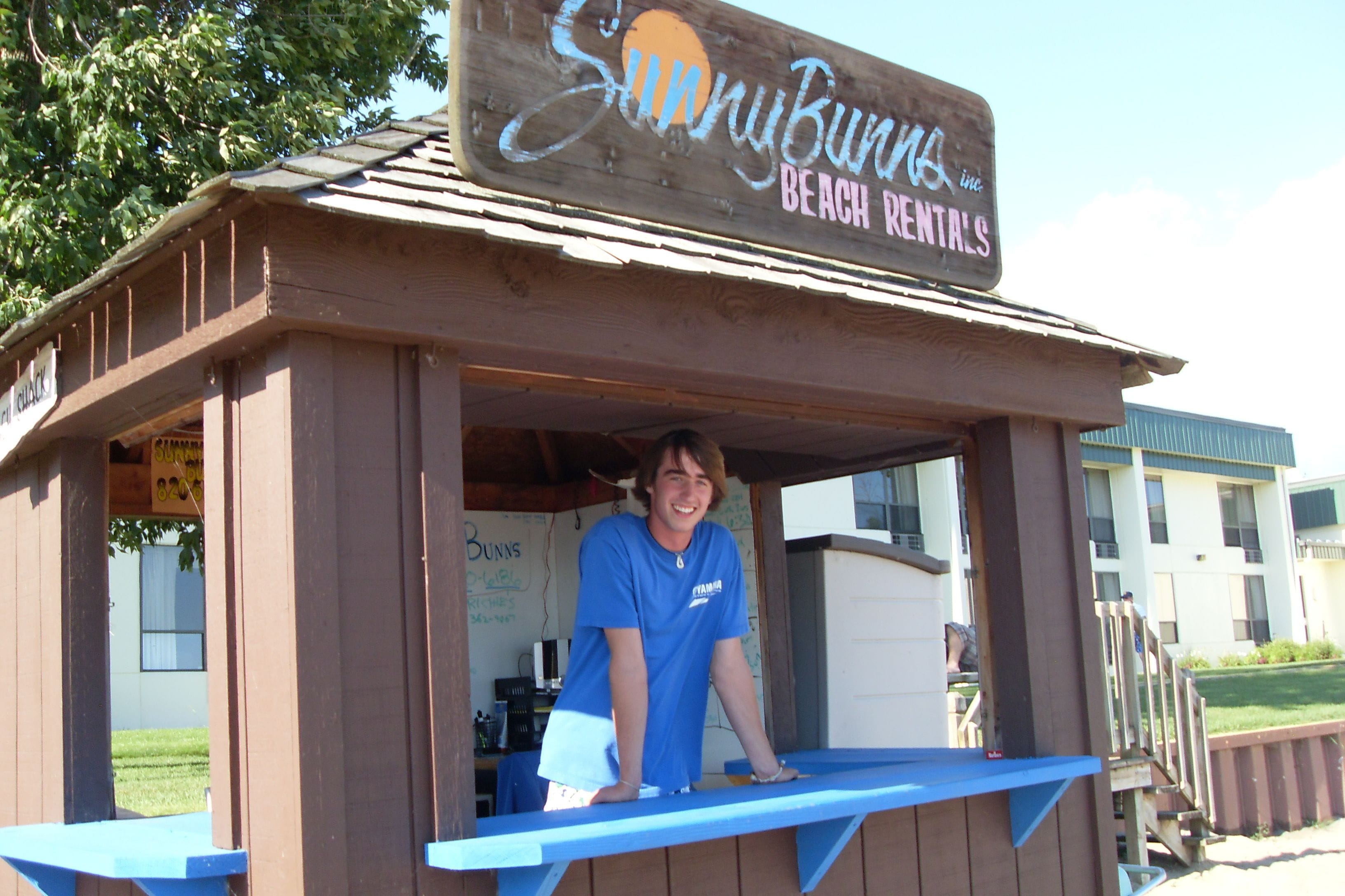 A wooden beach rental kiosk with a sign reading "SunnyBurns Beach Rentals."