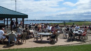 Un espace de restauration en plein air avec des tables et des chaises rondes, offrant une vue sur un plan d’eau et un pont.