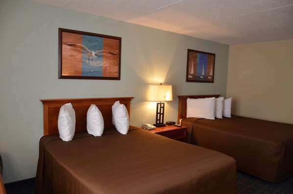 A hotel room with two beds, a nightstand with a lamp, and two framed pictures on the wall.