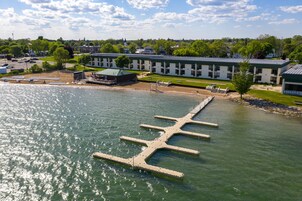 Un hotel frente al agua con un muelle que se adentra en el agua, un estacionamiento y un edificio con techo verde.