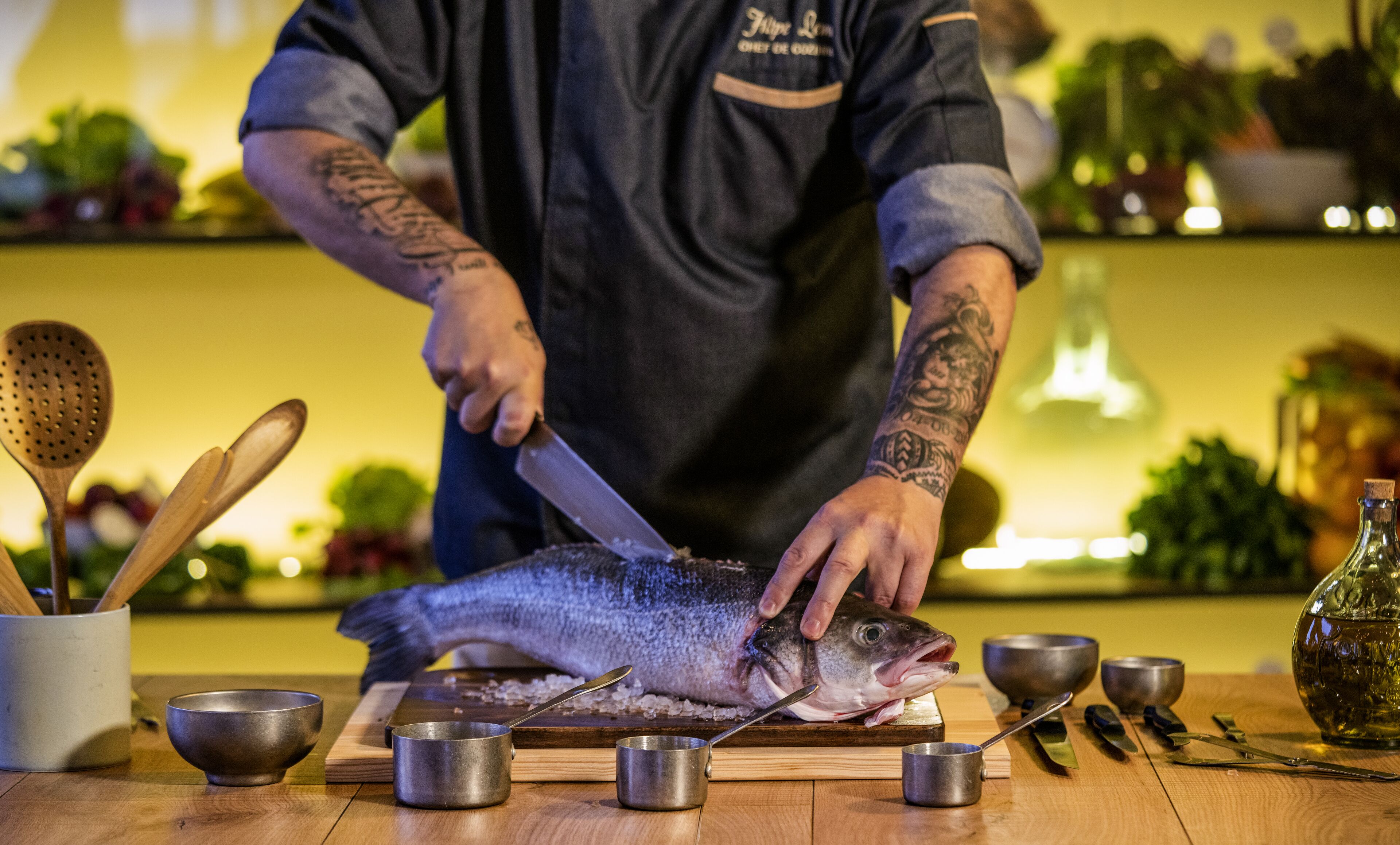 A chef preparing fish on a wooden cutting board with various kitchen utensils and bowls around.