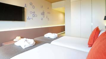 A modern hotel room with a bed, bedside tables, a flat-screen TV, and a wall with various icons.
