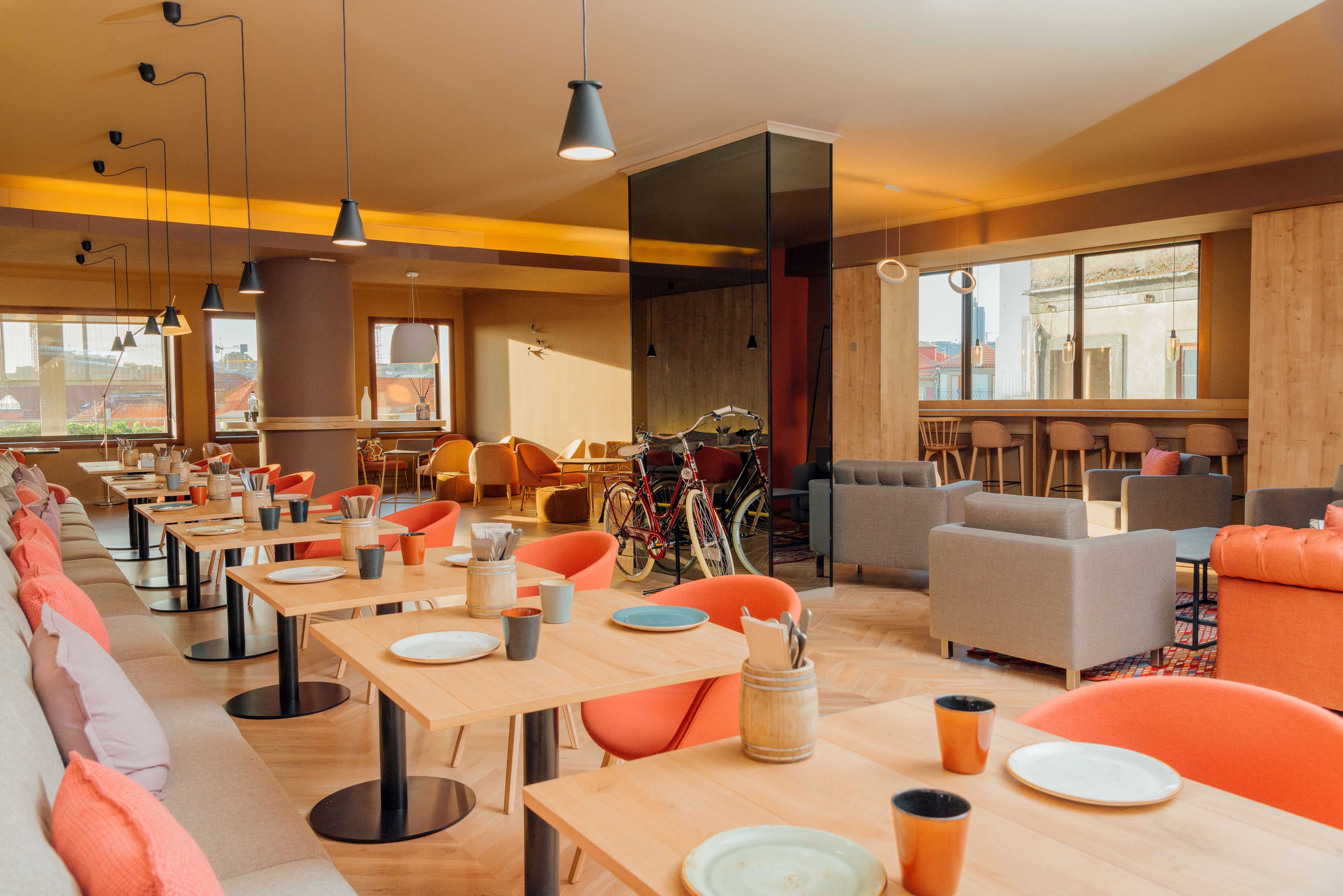 Zona pranzo moderna con diversi tavoli e sedie, una bicicletta e un'ampia finestra che offre vista sulla città.