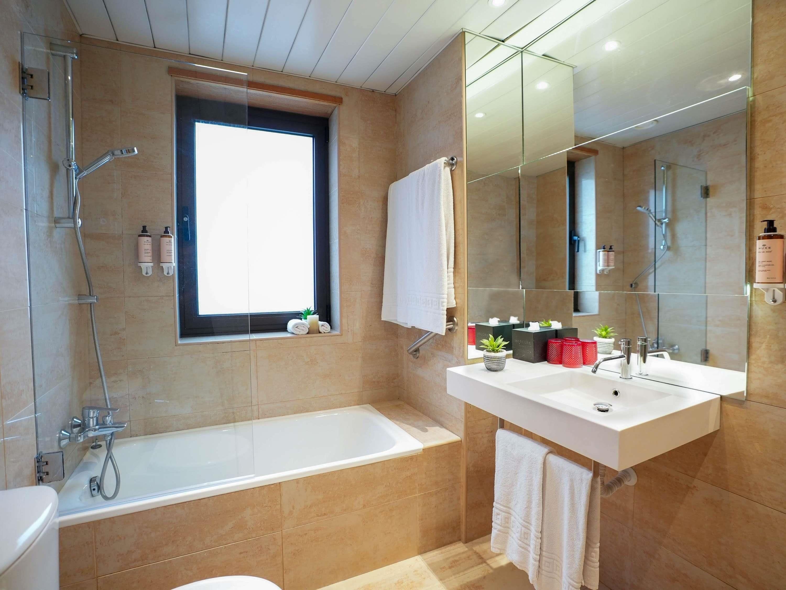 A modern bathroom with a bathtub, a large mirror, and a window.