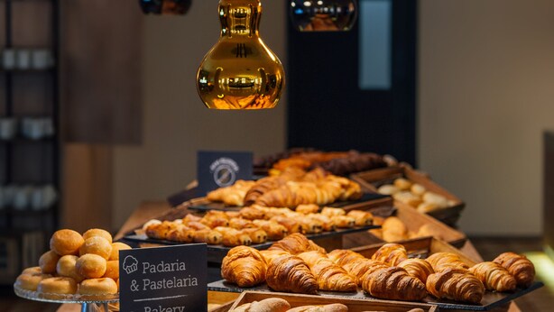A bakery display with pastries and bread, illuminated by hanging lights. - Mercure Porto Centro Santa Catarina (Porto)