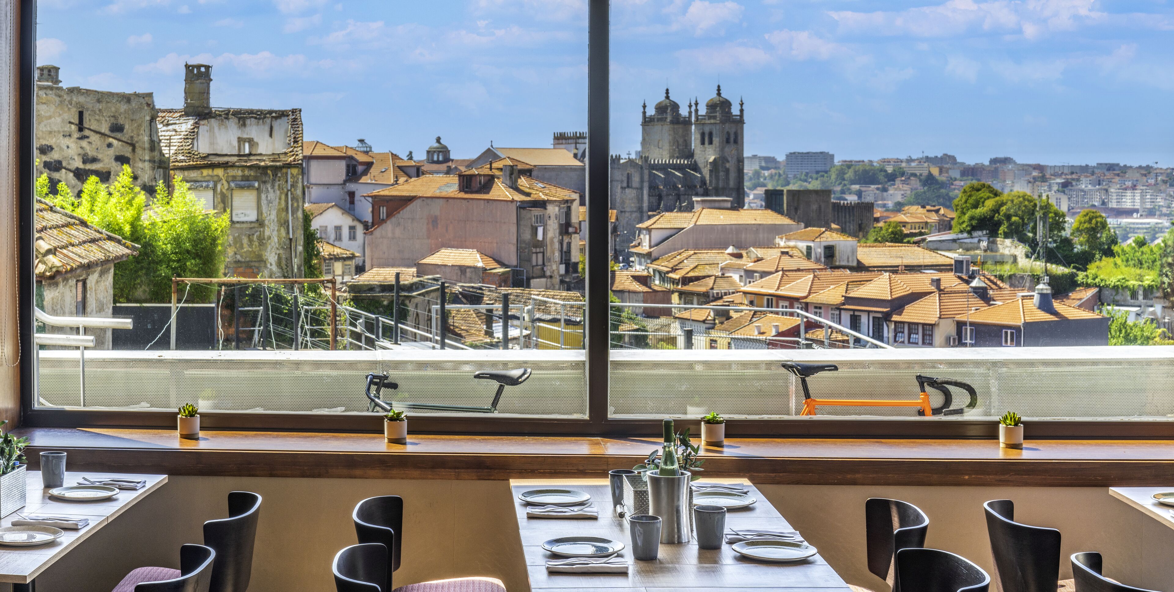 Un restaurante con vistas a edificios históricos y una iglesia. Las mesas están preparadas con platos y cubiertos.