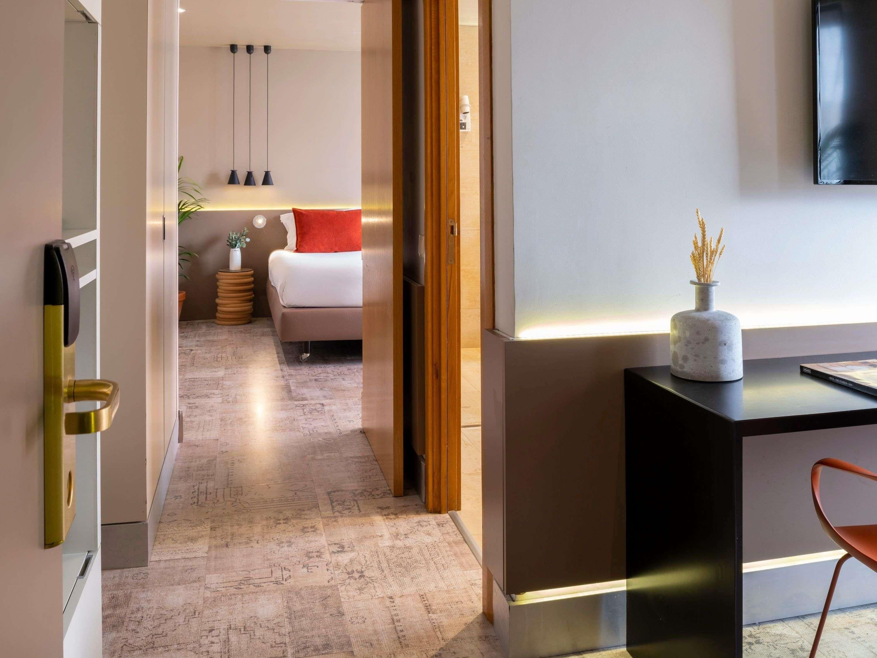 Habitació d'hotel moderna amb un llit, una taula de nit i un escriptori amb un vas.