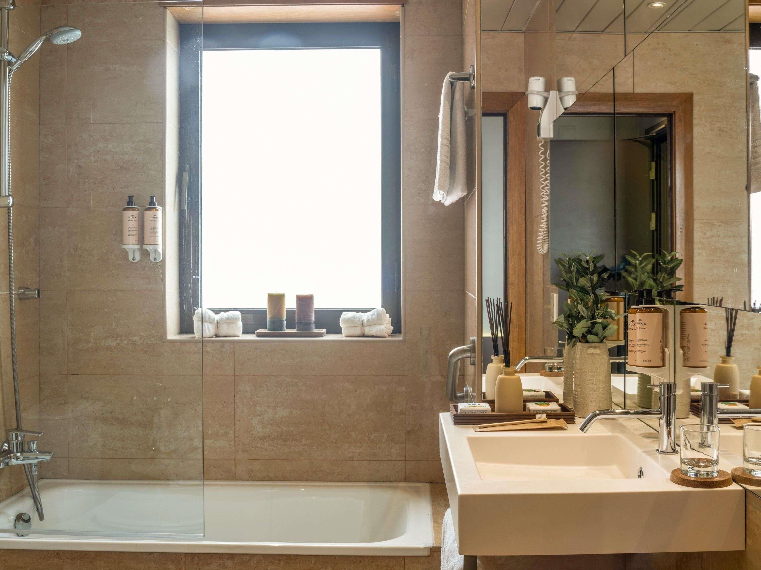 Un baño moderno con bañera, ventana, tocador con espejo y artículos de aseo.