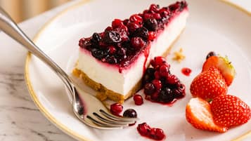 A slice of cheesecake with berries on a plate, accompanied by strawberries and a fork.