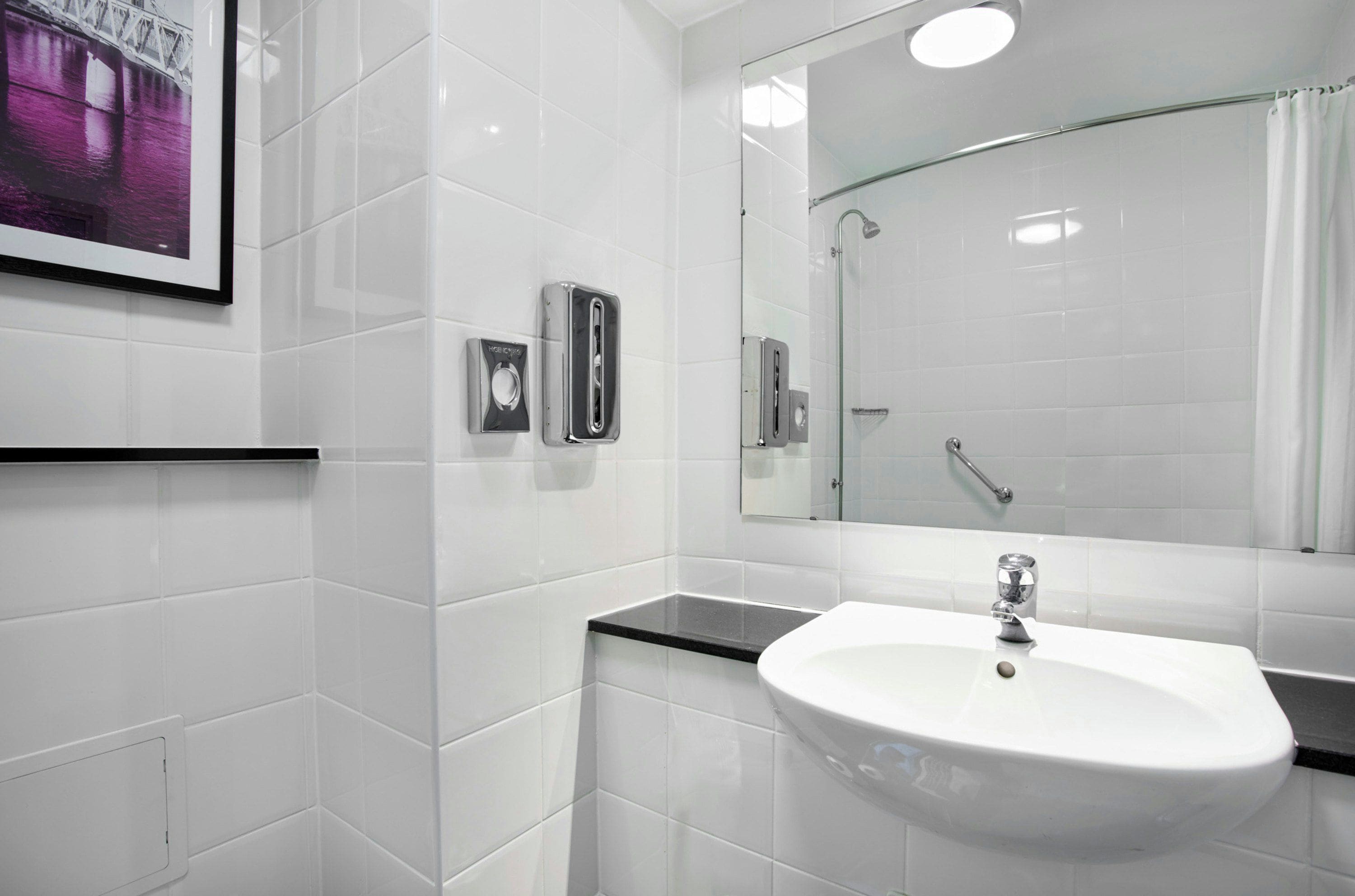 Ein modernes Badezimmer mit weißen Fliesen, einem weißen Waschbecken, einer Duschkabine aus Glas und einem gerahmten Bild an der Wand.