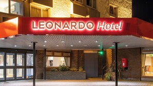 The exterior of the Leonardo Hotel with a prominent red sign, a brick facade, and a covered entrance area. - Leonardo Hotel Inverness (Inverness)