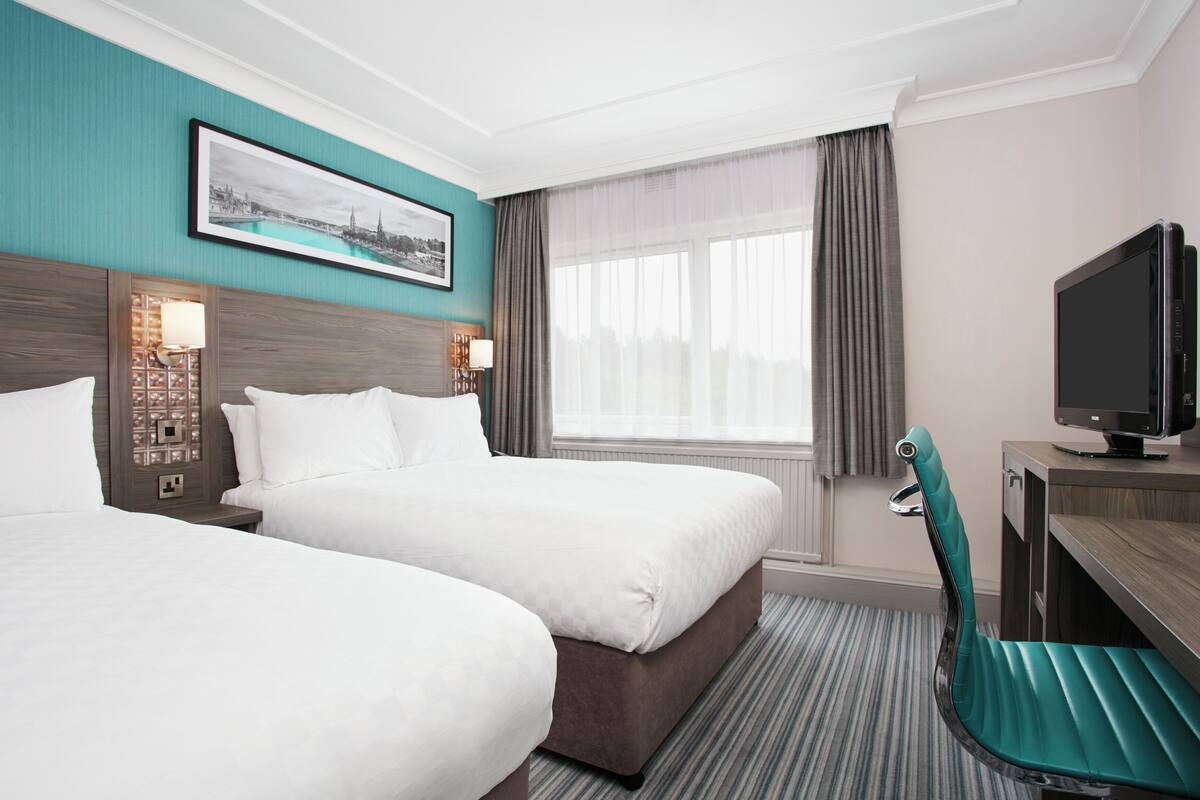 A hotel room with two beds, a television, a desk, and a window with curtains.