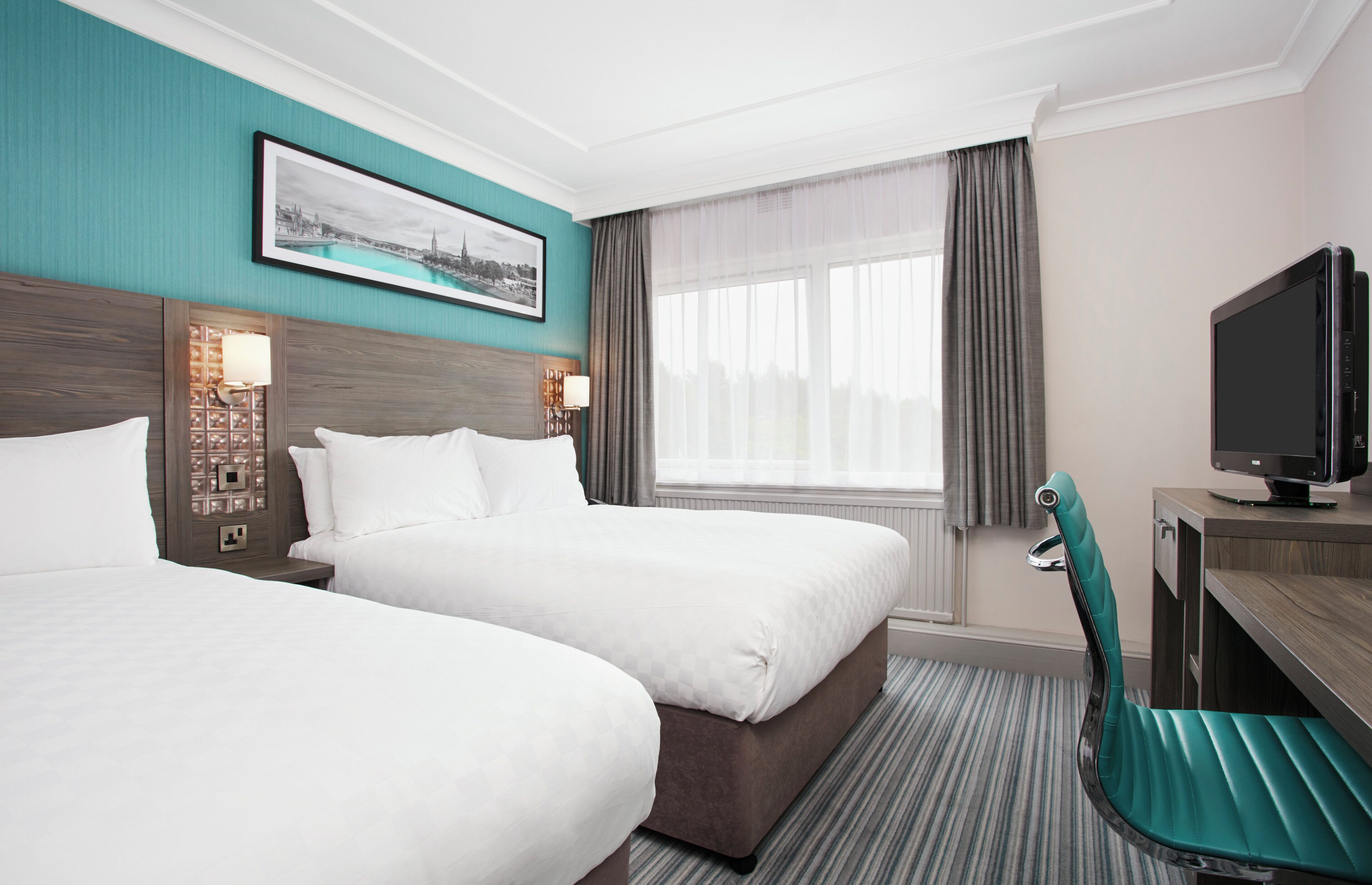 A hotel room with two beds, a television, a desk, and a window with curtains.