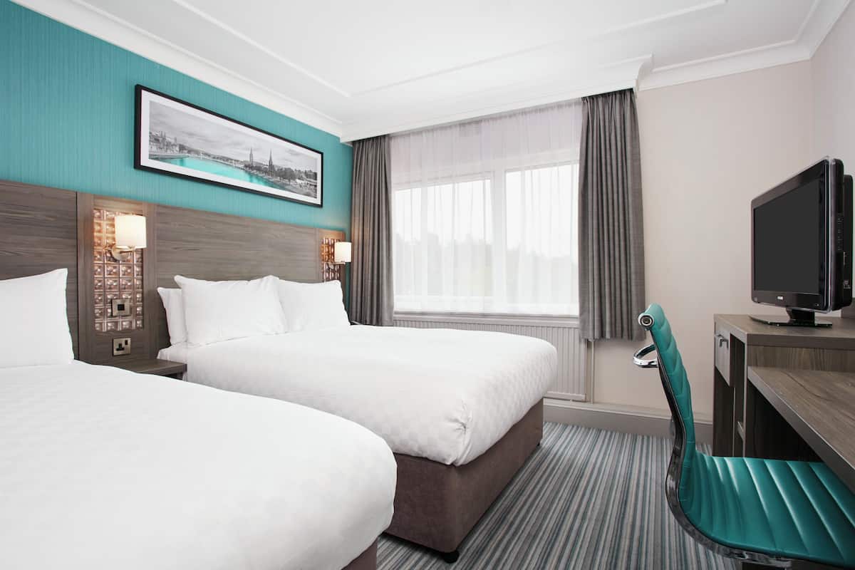 A hotel room with two beds, a television, a desk, and a window with curtains.