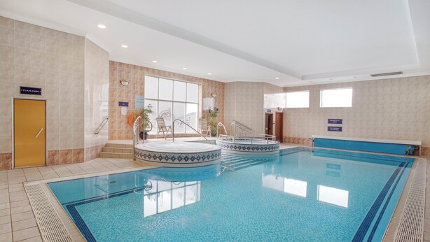 A large indoor swimming pool with two hot tubs, a sunlit room with a large window, and a sign indicating a steam room. - Leonardo Hotel Inverness (Inverness)
