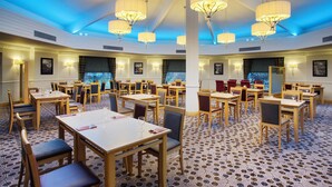 A spacious dining area with multiple tables and chairs, large chandeliers, and a patterned carpet. - Leonardo Hotel Inverness (Inverness)