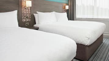 A hotel room with two beds, a nightstand, a wall-mounted lamp, and a window with curtains.