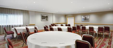 A conference room with round tables and red chairs, white tablecloths, and a carpeted floor.