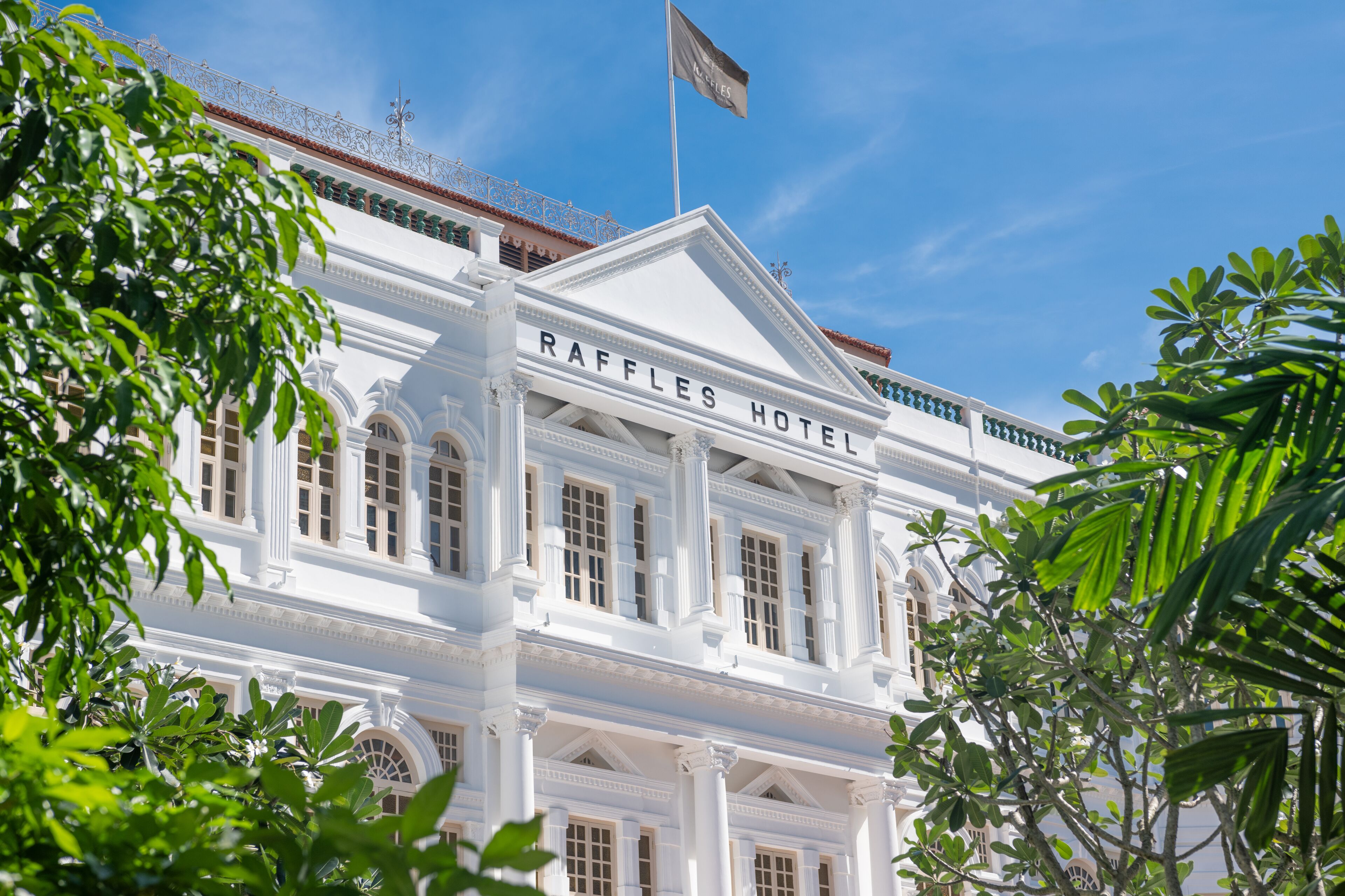 The Raffles Hotel with classical architecture, large windows, and a flag on top.