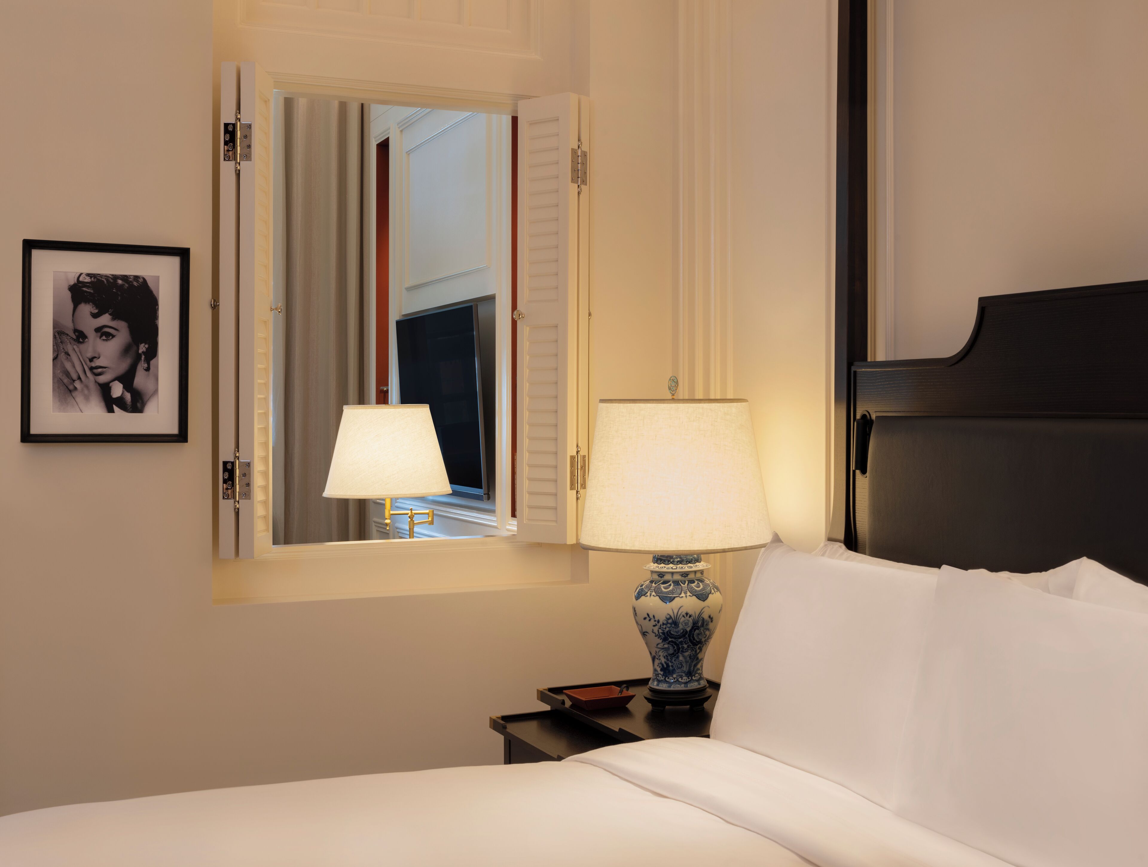 A hotel room with a bed, two bedside lamps, a framed picture on the wall, and a window with curtains.