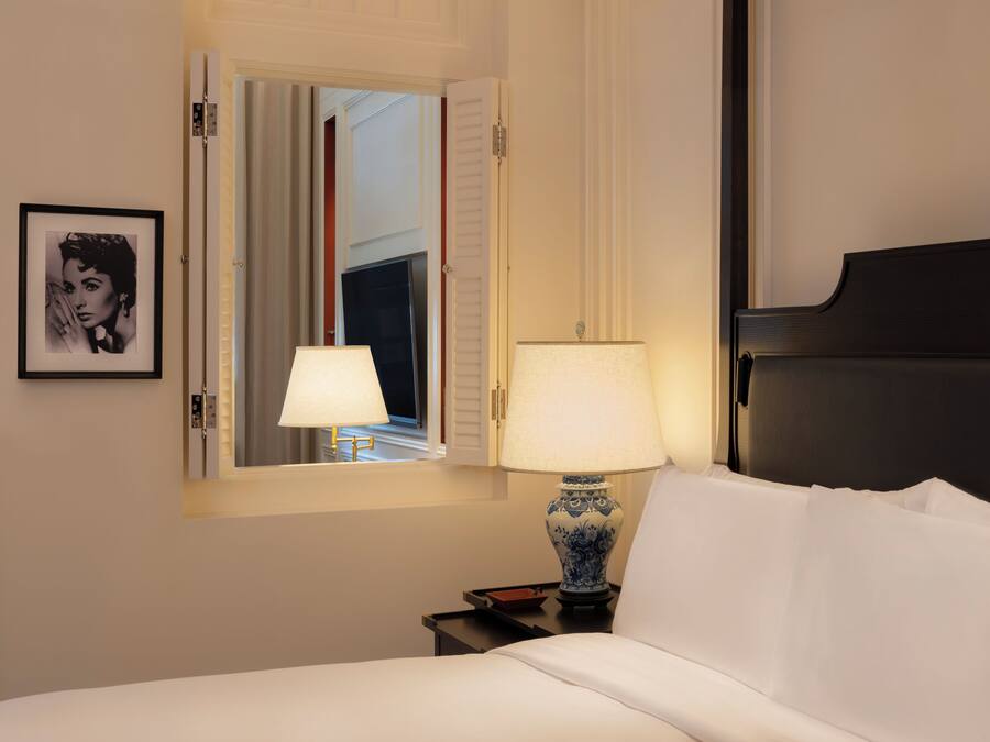 A hotel room with a bed, two bedside lamps, a framed picture on the wall, and a window with curtains.