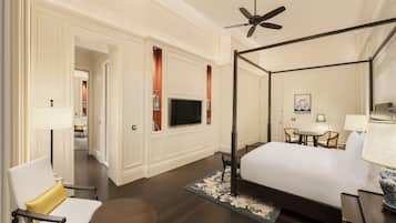 A hotel room with a four-poster bed, a television mounted on the wall, a dining area with a table and chairs, and a ceiling fan.