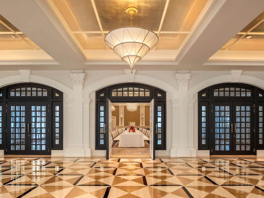 Un hall d’entrée spacieux doté d’un sol carrelé aux motifs géométriques, de trois portes en arc de cercle et d’un espace salon central agrémenté d’un lustre.