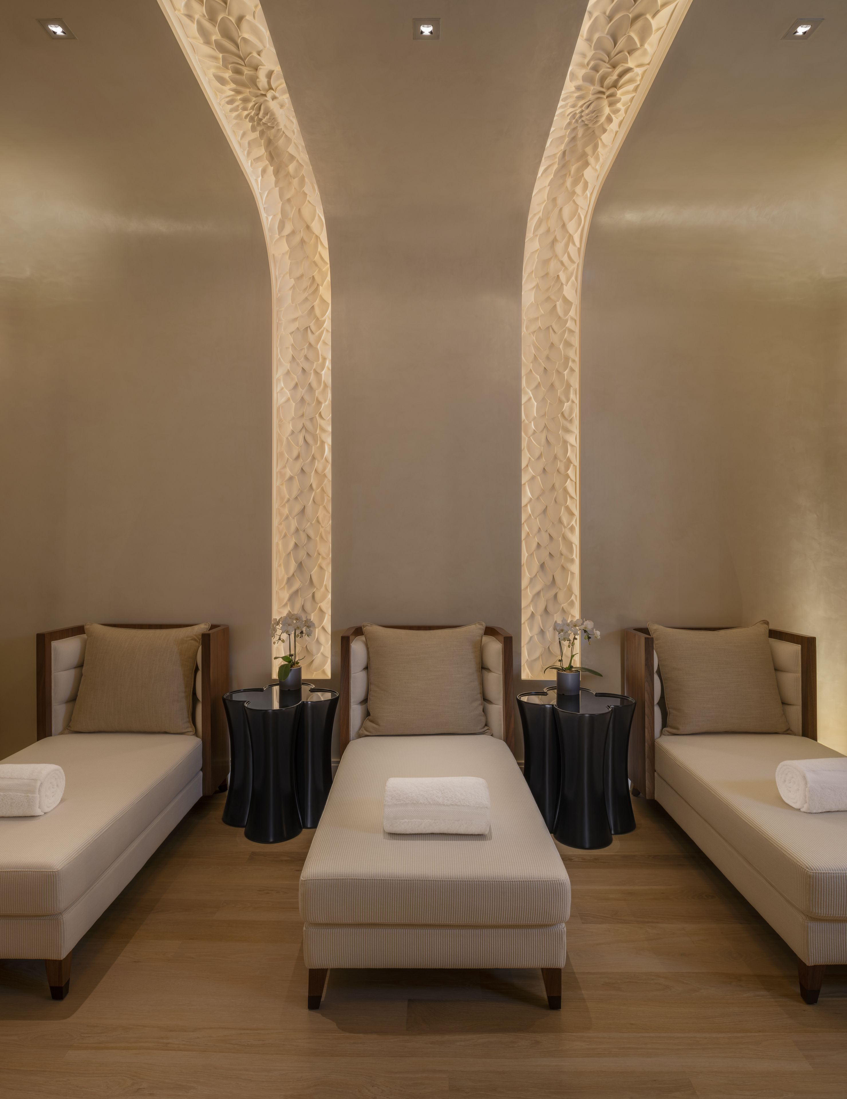 Habitación de hotel con dos camas individuales, un banco central y dos mesitas con plantas en macetas.