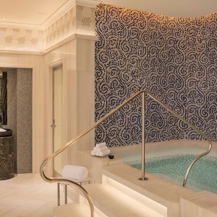 A luxurious bathroom with a marble bathtub, a glass-enclosed shower, and a decorative wall with a leaf pattern.