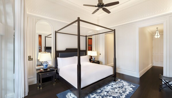 A four-poster canopy bed with a dark wooden frame and white bedding, flanked by nightstands with lamps and a vase.