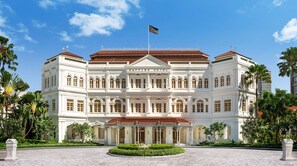 A large, white, colonial-style building with the name 'RAFFLES HOTEL' prominently displayed. It features a symmetrical facade with multiple windows and a central entrance.