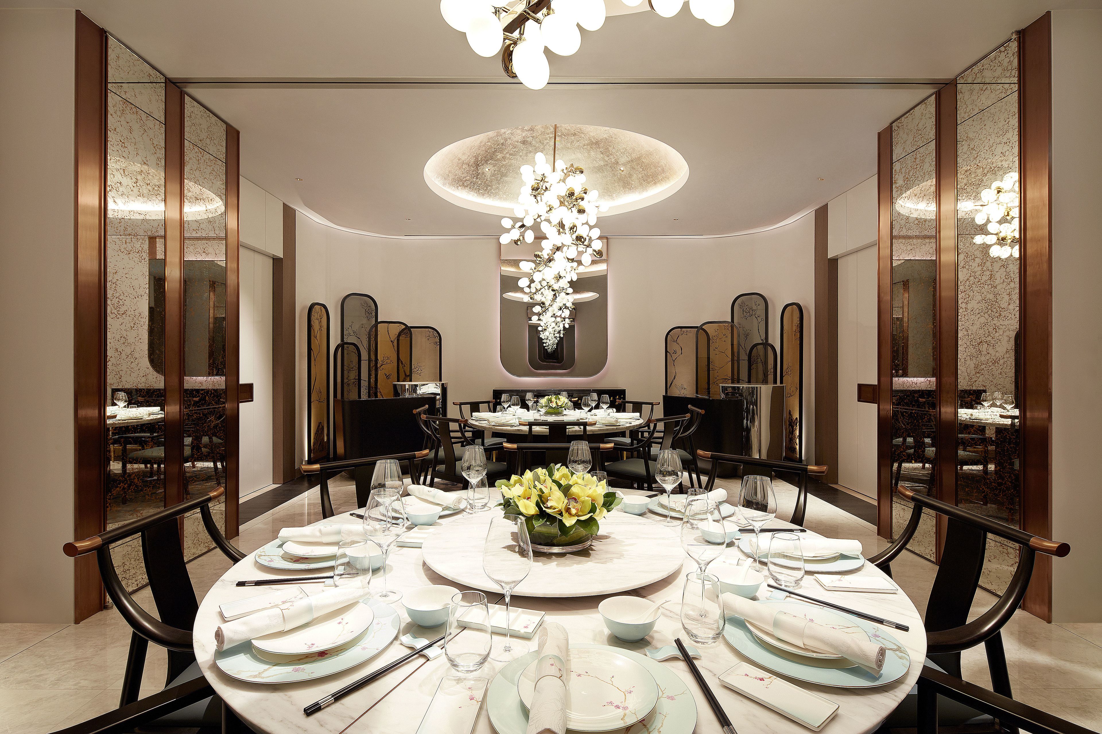 Un comedor formal con una mesa redonda dispuesta para una comida, rodeada de sillas, y un candelabro colgante.