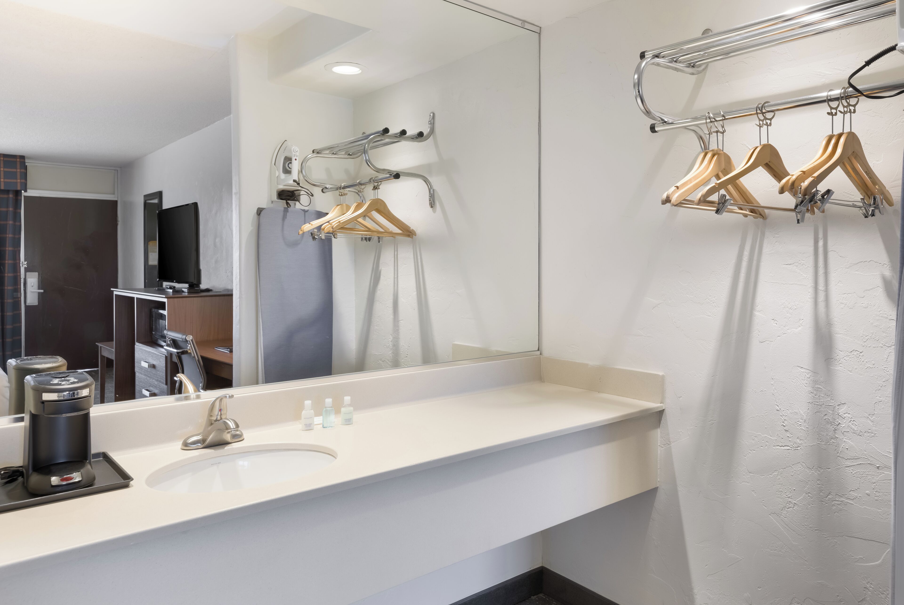 A modern bathroom with a white sink, a mirror, and a towel rack with wooden hangers.