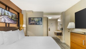 A hotel room with a large bed, a flat-screen TV mounted on the wall, a painting, a bathroom with a sink and mirror, and a wooden cabinet. - Best Western Queens Gold Coast (Bayside)