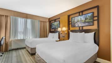 A hotel room with two beds, a desk, and a chair. There are two wall-mounted lamps and a large window with curtains.