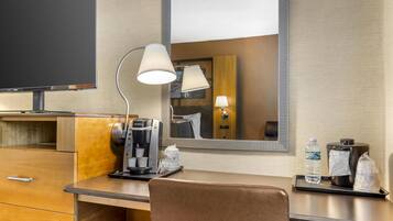 Ein Hotelzimmer mit einem Holztisch, einer Kaffeemaschine, einer Lampe, einem Spiegel und einem Fernseher.